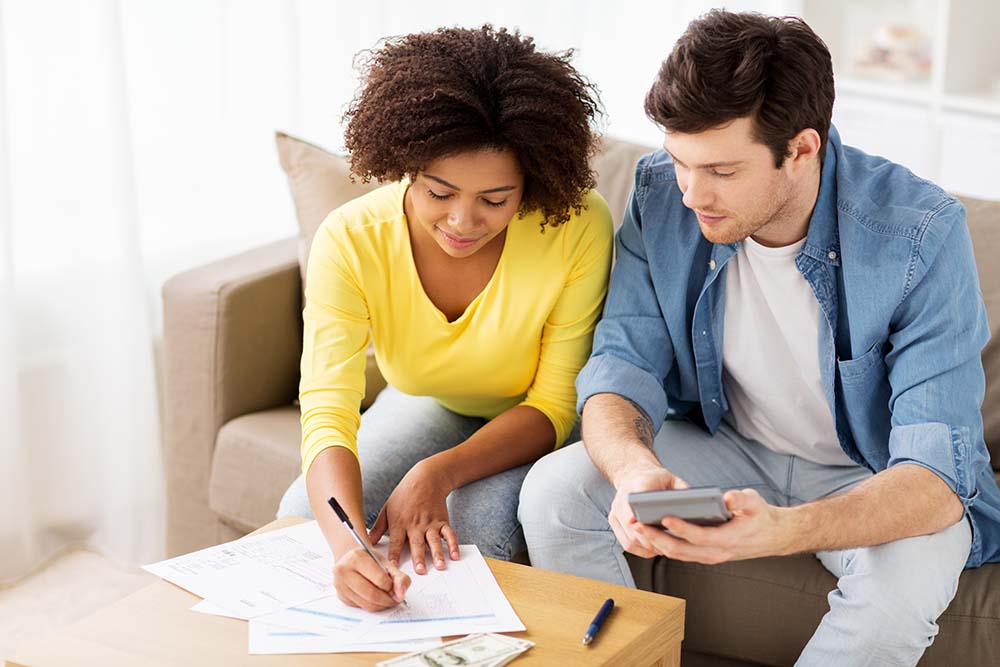man and woman sat on a couch, reviewing financees and bills with a calculator