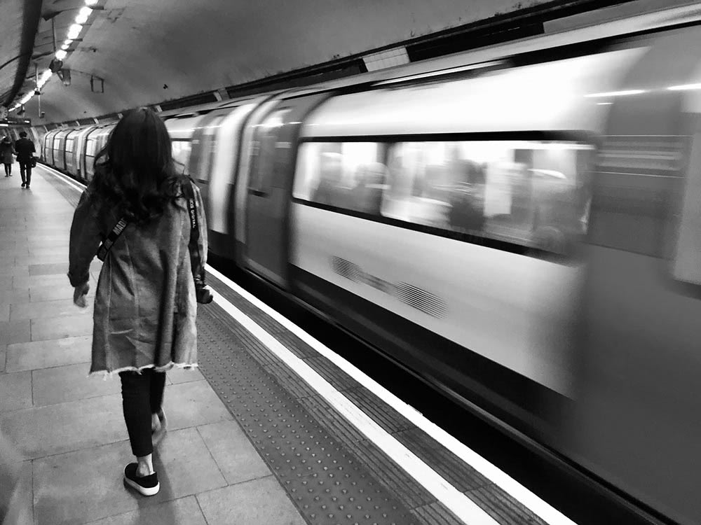 black and white photo of woman walking on a tube platform next to a moving train